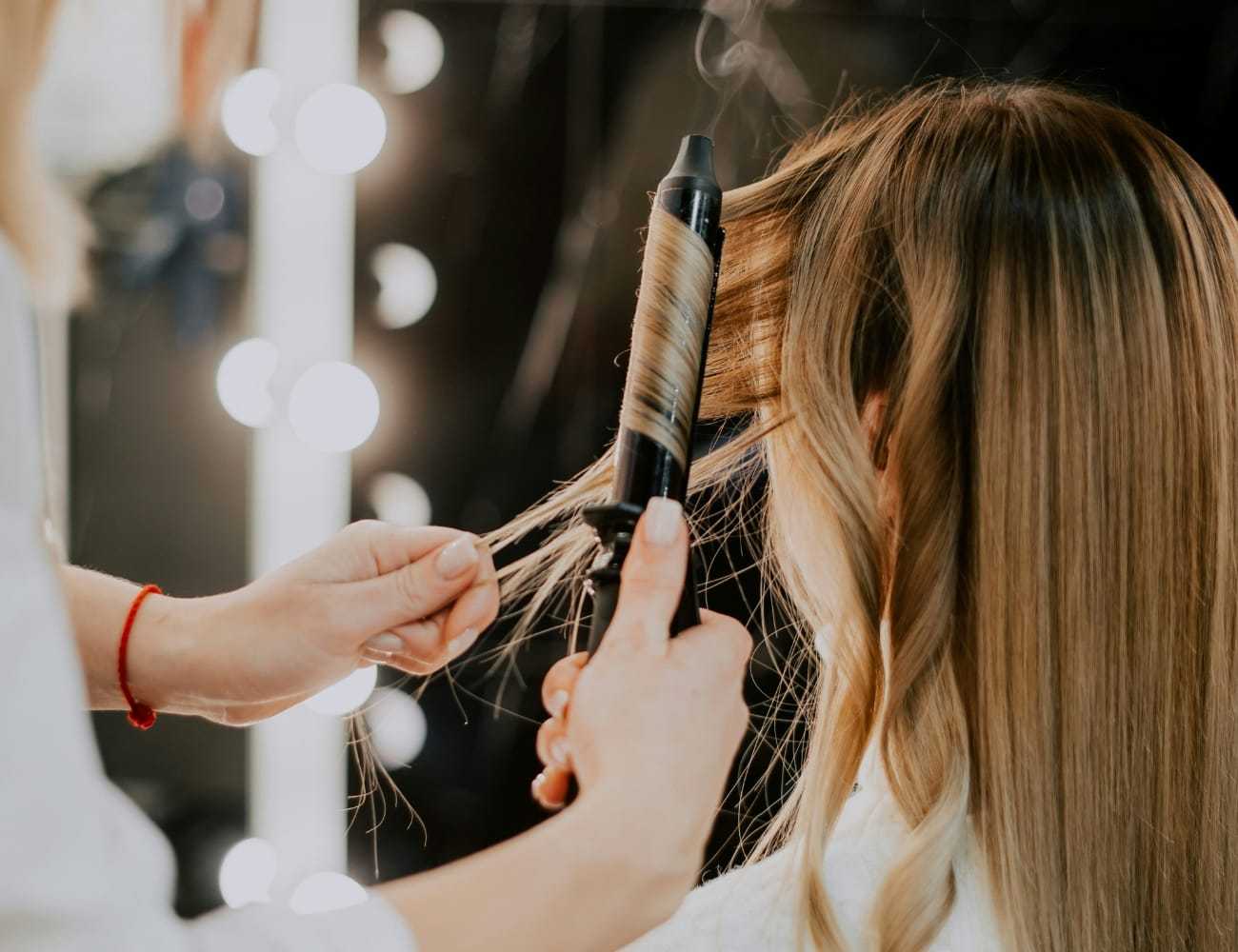 Hairdresser curling a woman's hair with a curling iron in a salon setting.