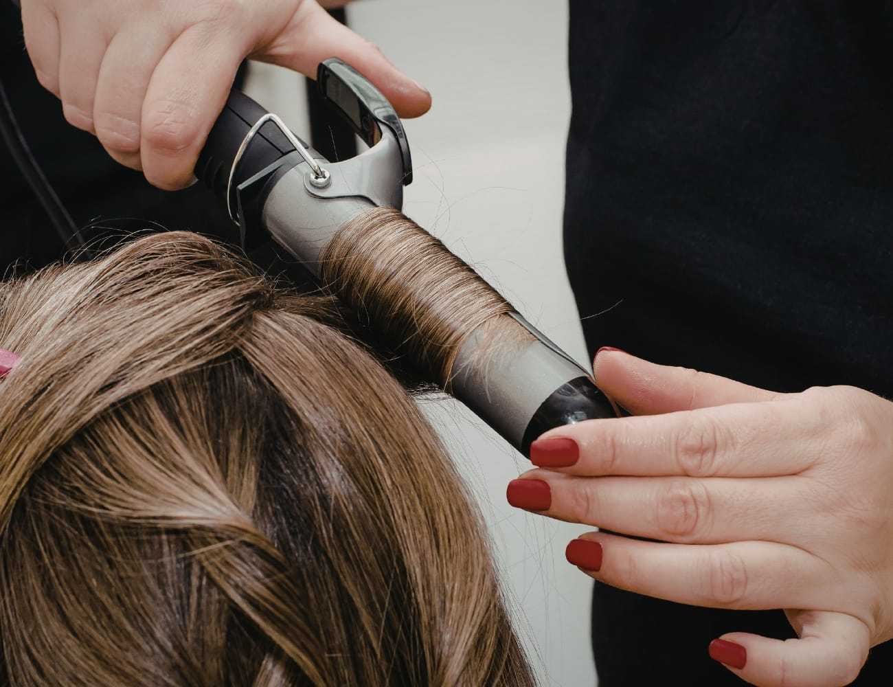 Curling hair with a curling iron, close-up of hands and tool in action.